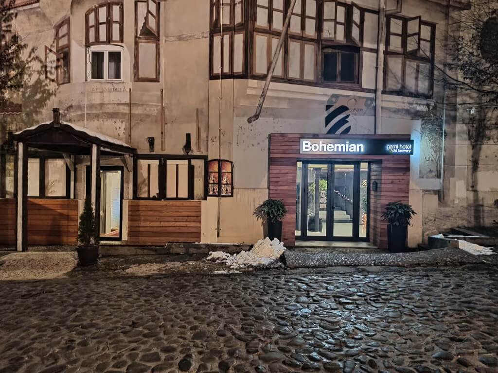 Ulaz u Hotel Bohemian Garni u Beogradu noću, sa osvetljenim znakom i kamenim kaldrmisanim putem ispred