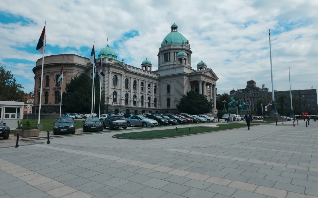 Zgrada Narodne skupštine u Beogradu sa zelenim kupolama i srpskim zastavama ispred, snimljena tokom dana