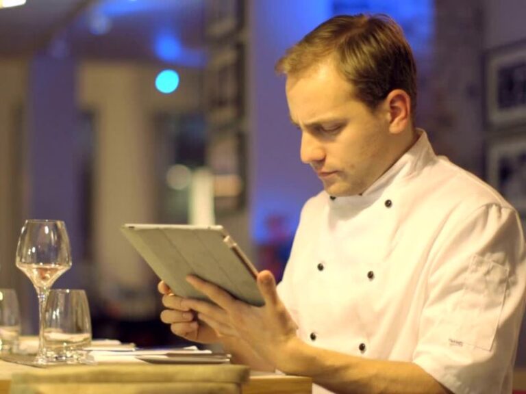 Šef kuhinje drži tablet u ruci i čita porudžbinu