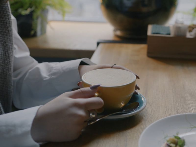 Devojka sedi u kafiću i drži u ruci šoljicu kafe